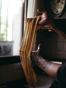 (Pasta artesanal): Fotografía gastronómica de proceso. Manos de chef manipulando pasta fresca artesanal, capturando la textura y el enfoque cinematográfico en cocina.