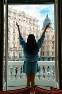 (Vistas al balcón): Modelo de espaldas asomada al balcón del Hotel Montera con vistas a la arquitectura icónica de la Gran Vía de Madrid. Fotografía de viajes y lujo.